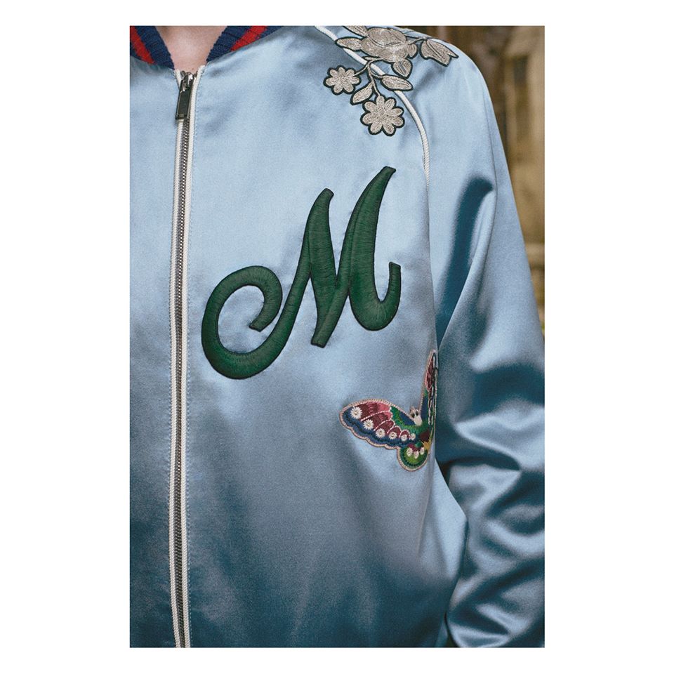 An embroidered patch letter on the chest of a silk bomber jacket with stripe Web trim.