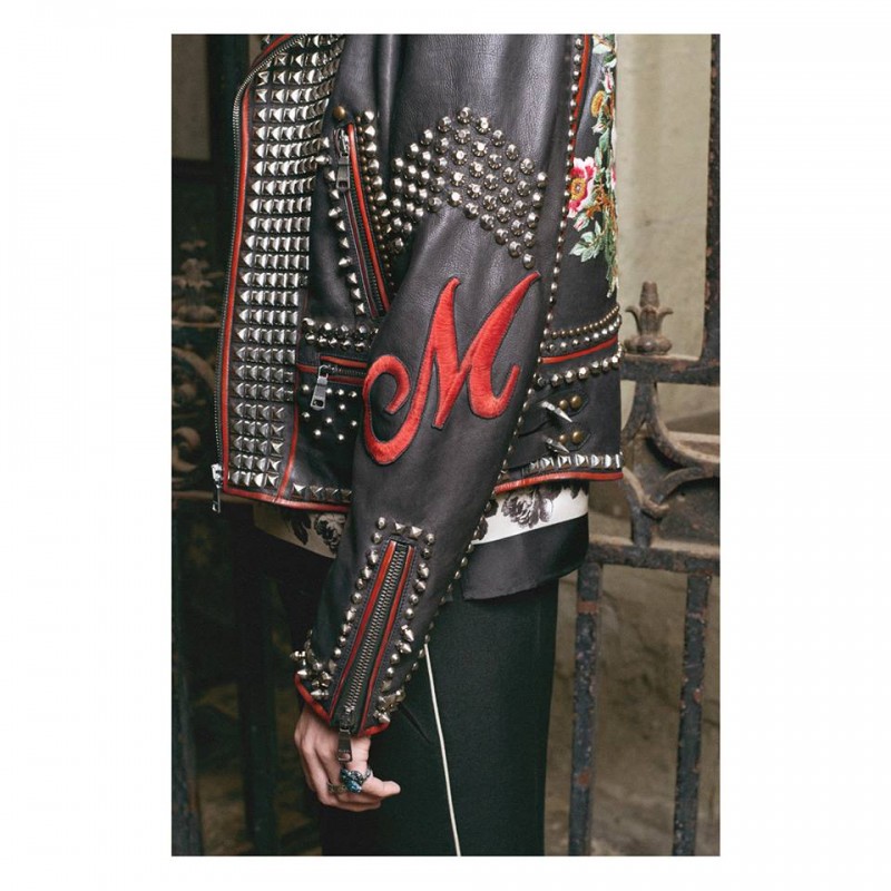 On a studded leather jacket, an embroidered patch letter is positioned on the sleeve